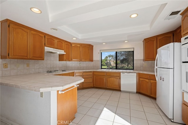 2207 Inverness Ct, Oxnard, CA 93036 - kitchen with white appliances, a tray ceiling, tile countertops, under cabinet range hood, and recessed lighting