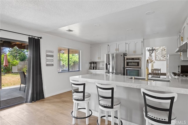 7209 Copper Creek Way, Bakersfield, CA 93308 - kitchen featuring appliances with stainless steel finishes, a peninsula, light wood-style floors, white cabinetry, and a breakfast bar area