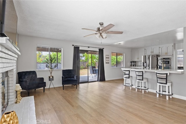 7209 Copper Creek Way, Bakersfield, CA 93308 - living room with a fireplace, ceiling fan, light wood-type flooring, a textured ceiling, and baseboards