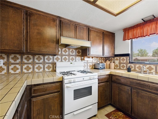 20654 Ottawa Rd, Apple Valley, CA 92308 - kitchen with white range with gas stovetop, tile countertops, under cabinet range hood, backsplash, and dark brown cabinets