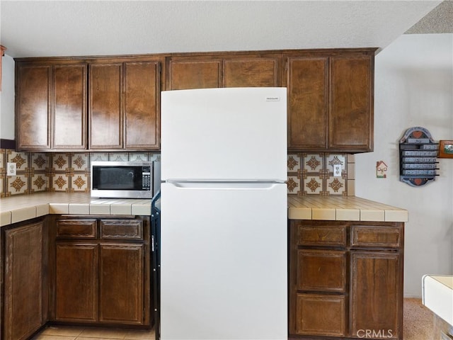 20654 Ottawa Rd, Apple Valley, CA 92308 - kitchen featuring freestanding refrigerator, tile counters, stainless steel microwave, and dark brown cabinets