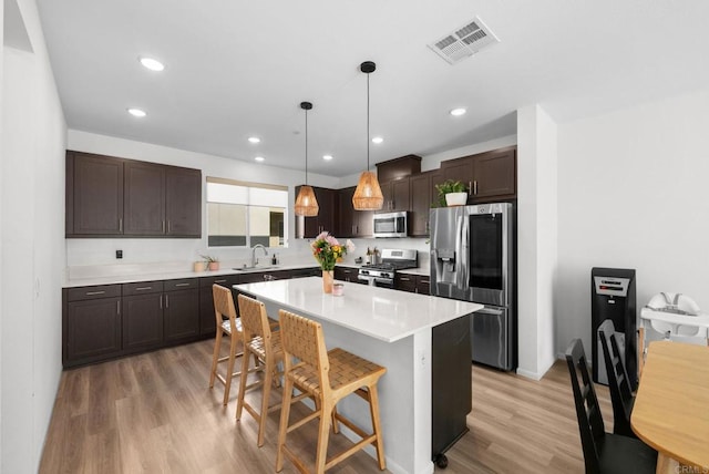 5485 Seacliff Pl Unit 106, San Diego, CA 92154 - kitchen featuring appliances with stainless steel finishes, a sink, dark brown cabinets, light wood-type flooring, and a breakfast bar area