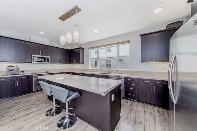 9213 Sunshine Pl, Downey, CA 90240 - kitchen featuring appliances with stainless steel finishes, light wood-style flooring, light countertops, a center island, and a breakfast bar