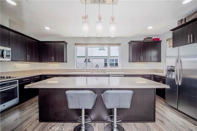 9213 Sunshine Pl, Downey, CA 90240 - kitchen with stainless steel appliances, light countertops, dark brown cabinetry, a kitchen island, and light wood-type flooring