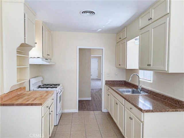 812 Wilson Ave, Bakersfield, CA 93308 - kitchen with a sink, white gas range oven, under cabinet range hood, light tile patterned flooring, and baseboards
