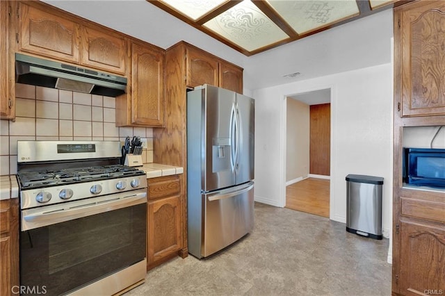 19055 Seaforth St, Hesperia, CA 92345 - kitchen featuring stainless steel appliances, under cabinet range hood, tile counters, decorative backsplash, and brown cabinets