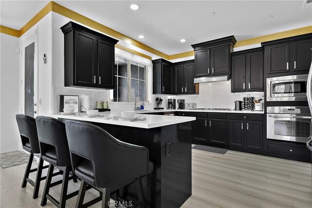 43228 Bacino Ct, Indio, CA 92203 - kitchen featuring stainless steel appliances, dark cabinetry, light wood-style floors, a breakfast bar area, and light countertops
