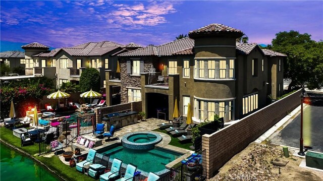 43228 Bacino Ct, Indio, CA 92203 - back of house at dusk with a balcony, stucco siding, a patio, a tiled roof, and a pool with connected hot tub