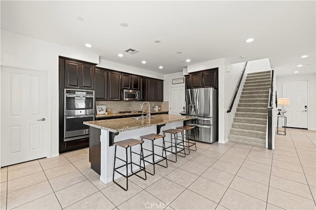 29015 Ridgecrest Ct, Valencia, CA 91354 - kitchen featuring stainless steel appliances, light tile patterned flooring, a breakfast bar area, a kitchen island with sink, and decorative backsplash