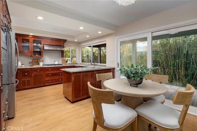 16561 Wanderer Ln, Huntington Beach, CA 92649 - kitchen with light wood finished floors, under cabinet range hood, appliances with stainless steel finishes, brown cabinetry, and glass insert cabinets