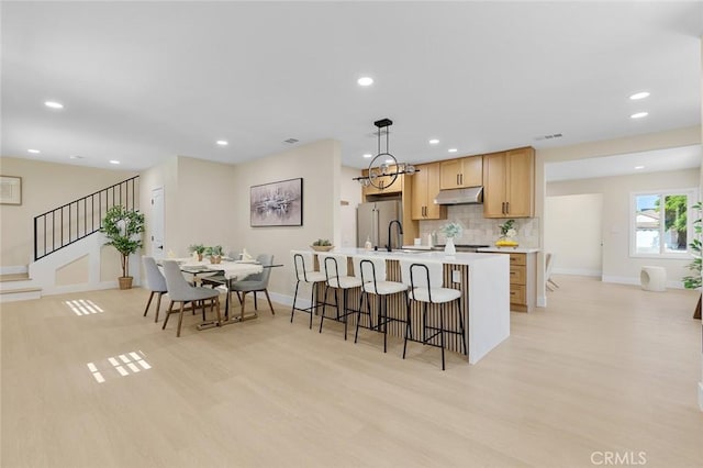 11091 Ranger Dr, Los Alamitos, CA 90720 - kitchen with under cabinet range hood, light wood-style floors, freestanding refrigerator, a kitchen breakfast bar, and light brown cabinetry