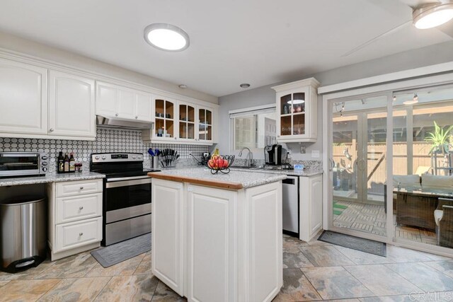 264 Espanas Gln, Escondido, CA 92026 - kitchen featuring appliances with stainless steel finishes, under cabinet range hood, white cabinetry, tasteful backsplash, and glass insert cabinets