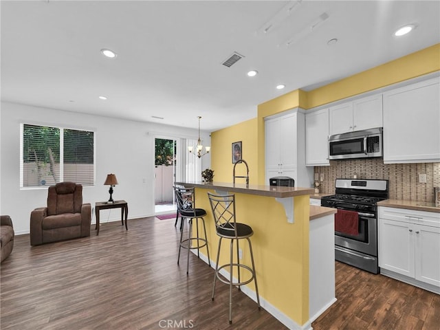 12347 N Aragon Way, Sylmar, CA 91342 - kitchen featuring appliances with stainless steel finishes, dark wood-style floors, a kitchen breakfast bar, decorative backsplash, and white cabinets