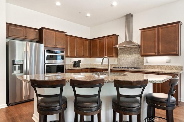 24190 Evesong Dr, Corona, CA 92883 - kitchen featuring stainless steel appliances, wall chimney range hood, a sink, a center island with sink, and dark wood finished floors