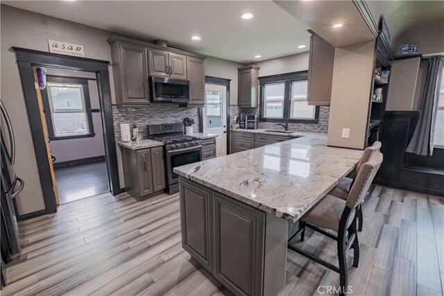 5837 Esperanza Ave, Whittier, CA 90606 - kitchen featuring stainless steel appliances, a breakfast bar area, light wood-style flooring, light stone counters, and a peninsula