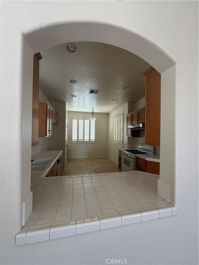14543 Handsdale St, Adelanto, CA 92301 - kitchen featuring gas range gas stove, arched walkways, brown cabinets, dishwasher, and hanging light fixtures