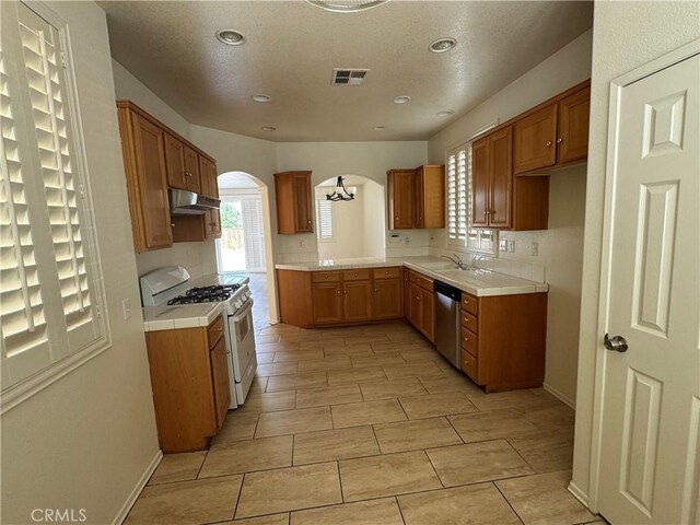 14543 Handsdale St, Adelanto, CA 92301 - kitchen with white gas stove, dishwasher, under cabinet range hood, tile countertops, and arched walkways