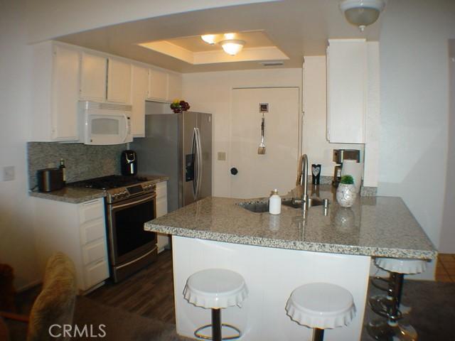 1412 Colonial Way, San Jacinto, CA 92583 - kitchen with white microwave, stainless steel range oven, a peninsula, and white cabinetry