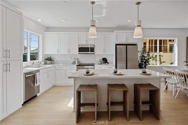 415 E 220th St, Carson, CA 90745 - kitchen featuring appliances with stainless steel finishes, white cabinetry, a sink, a center island, and light wood finished floors