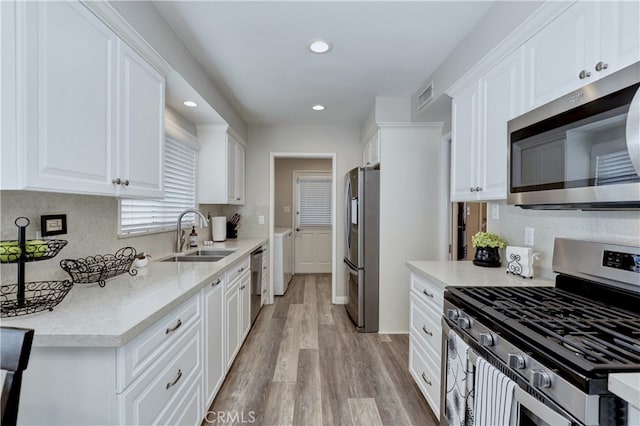 14522 San Feliciano Ln, Mirada, CA 90638 - kitchen featuring appliances with stainless steel finishes, a sink, washing machine and dryer, white cabinets, and recessed lighting