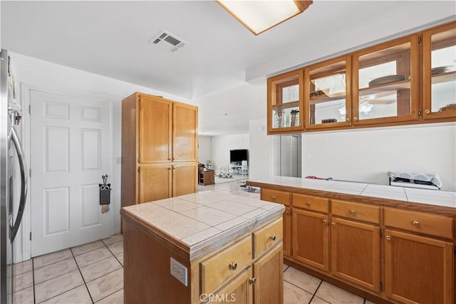 9824 Evelyn Ave, California City, CA 93505 - kitchen with tile countertops, light tile patterned floors, glass insert cabinets, and brown cabinets