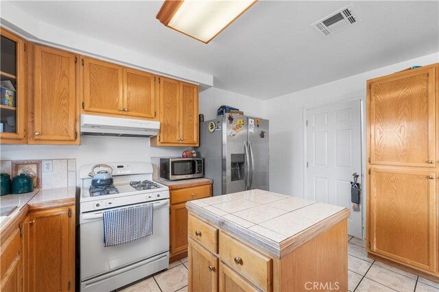 9824 Evelyn Ave, California City, CA 93505 - kitchen featuring stainless steel appliances, under cabinet range hood, tile countertops, and light tile patterned floors