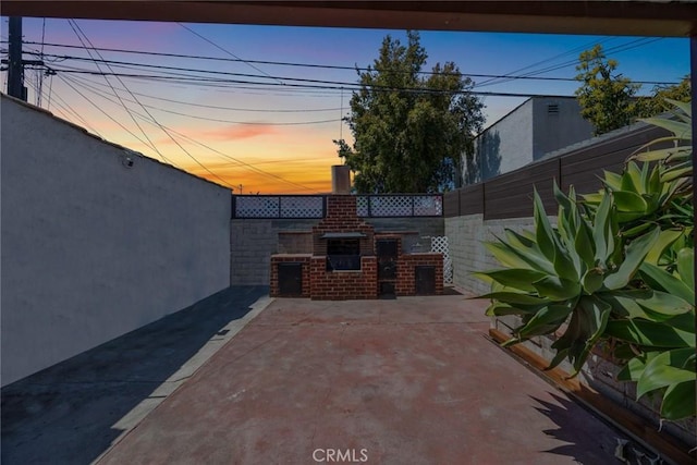 7037 Cimarron St, Los Angeles, CA 90047 - patio terrace at dusk featuring a fenced backyard, a patio area, and a fireplace