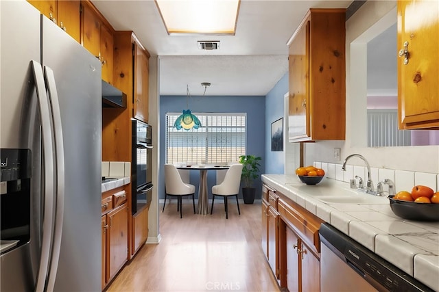 1254 Fieldgate Ave, Hacienda Heights, CA 91745 - kitchen with appliances with stainless steel finishes, a warming drawer, brown cabinetry, light wood-type flooring, and tile countertops