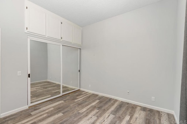 8328 Regents Rd Unit 1K, San Diego, CA 92122 - unfurnished bedroom with wood finished floors, baseboards, a closet, and a textured ceiling