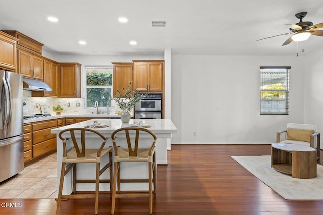 3806 Golden Pond Dr, Camarillo, CA 93012 - kitchen featuring appliances with stainless steel finishes, under cabinet range hood, a ceiling fan, brown cabinetry, and backsplash