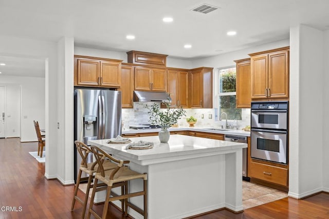 3806 Golden Pond Dr, Camarillo, CA 93012 - kitchen featuring appliances with stainless steel finishes, under cabinet range hood, a sink, tasteful backsplash, and light countertops