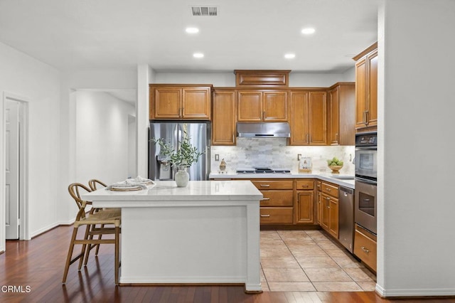 3806 Golden Pond Dr, Camarillo, CA 93012 - kitchen with appliances with stainless steel finishes, under cabinet range hood, backsplash, a center island, and brown cabinets