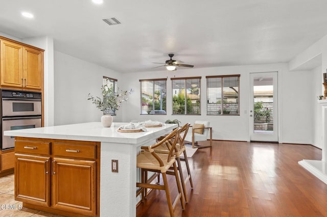 3806 Golden Pond Dr, Camarillo, CA 93012 - kitchen featuring stainless steel double oven, light countertops, ceiling fan, a breakfast bar area, and light wood-style flooring