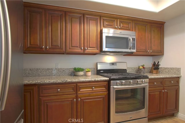 9009 Buckles St, Downey, CA 90241 - kitchen featuring stainless steel appliances, brown cabinets, and light stone counters