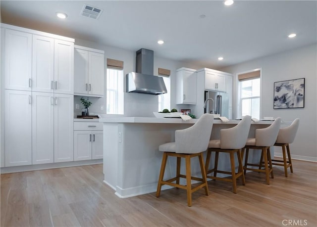 21 Welltree Way, Rancho Mission Viejo, CA 92694 - kitchen with wall chimney exhaust hood, a kitchen bar, light wood-style floors, white cabinetry, and recessed lighting