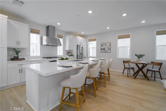 21 Welltree Way, Rancho Mission Viejo, CA 92694 - kitchen featuring wall chimney exhaust hood, a center island with sink, a kitchen bar, light countertops, and white cabinetry