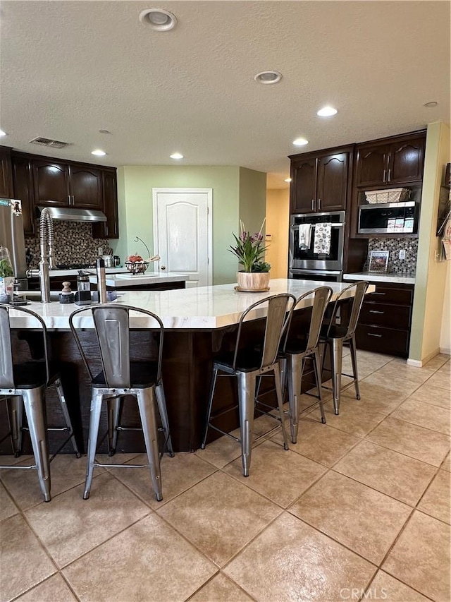 8843 San Diego Dr, Yucca Valley, CA 92284 - kitchen featuring under cabinet range hood, appliances with stainless steel finishes, backsplash, a breakfast bar, and recessed lighting