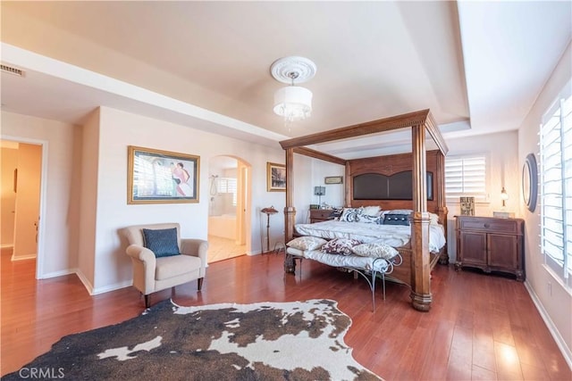668 Corte Sol, Camarillo, CA 93010 - bedroom featuring a tray ceiling, arched walkways, wood-type flooring, baseboards, and connected bathroom