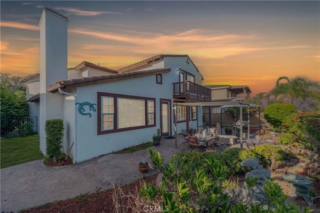 668 Corte Sol, Camarillo, CA 93010 - back of house at dusk featuring a balcony, a patio, stucco siding, a chimney, and a tile roof