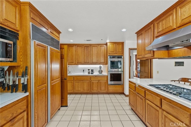 52 Hidden Valley Rd, Monrovia, CA 91016 - kitchen with appliances with stainless steel finishes, under cabinet range hood, light countertops, light tile patterned floors, and brown cabinetry