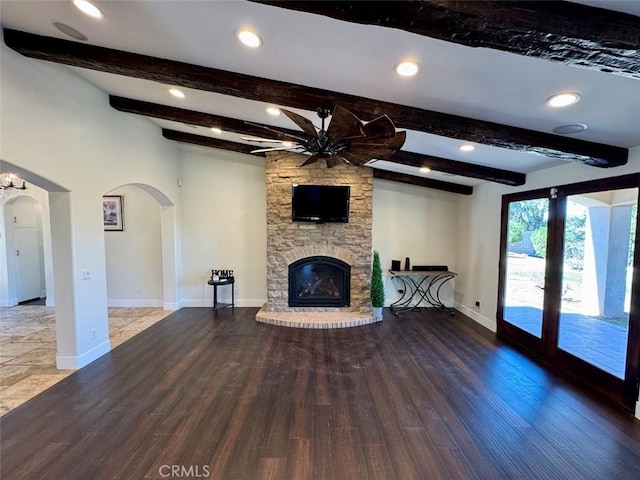 1415 Via Vallarta, Riverside, CA 92506 - unfurnished living room with a ceiling fan, arched walkways, wood finished floors, a stone fireplace, and beam ceiling