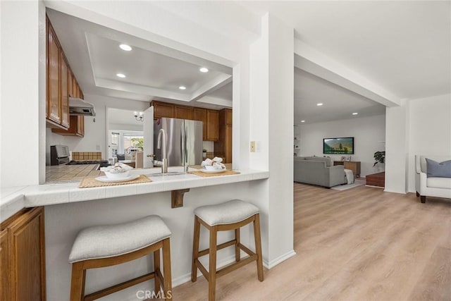 915 W Solano St, Upland, CA 91784 - kitchen featuring freestanding refrigerator, brown cabinets, exhaust hood, a breakfast bar, and recessed lighting