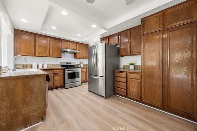 915 W Solano St, Upland, CA 91784 - kitchen with appliances with stainless steel finishes, under cabinet range hood, tile counters, a raised ceiling, and light wood-style floors