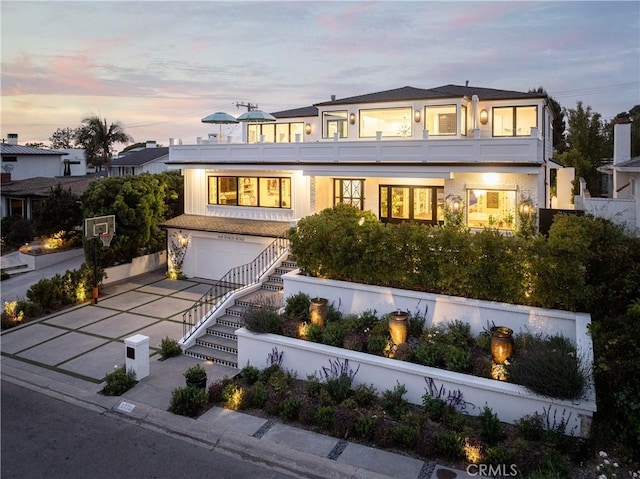 1110 Kings Rd, Newport Beach, CA 92663 - back of property at dusk with a garage, a balcony, and driveway