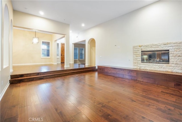 12160 Glines Ct, Tustin, CA 92782 - unfurnished living room featuring a stone fireplace, arched walkways, wood-type flooring, and baseboards