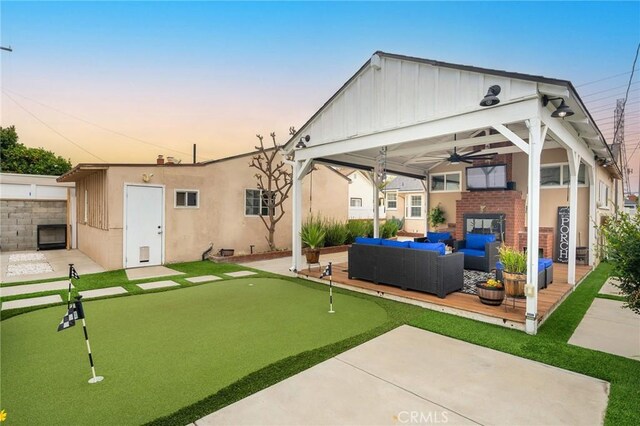 6003 Eastbrook Ave, Lakewood, CA 90713 - back of house at dusk featuring a putting area, an outdoor hangout area, board and batten siding, and a patio area