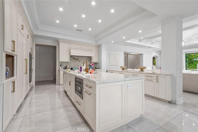 25548 Kingston Ct, Calabasas, CA 91302 - kitchen with a raised ceiling, a center island with sink, backsplash, light stone countertops, and custom exhaust hood