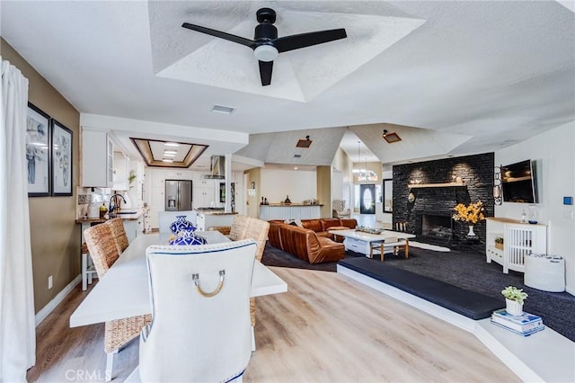 18016 Mariner Dr, Victorville, CA 92395 - dining space with light wood finished floors, a large fireplace, a tray ceiling, a ceiling fan, and a textured ceiling