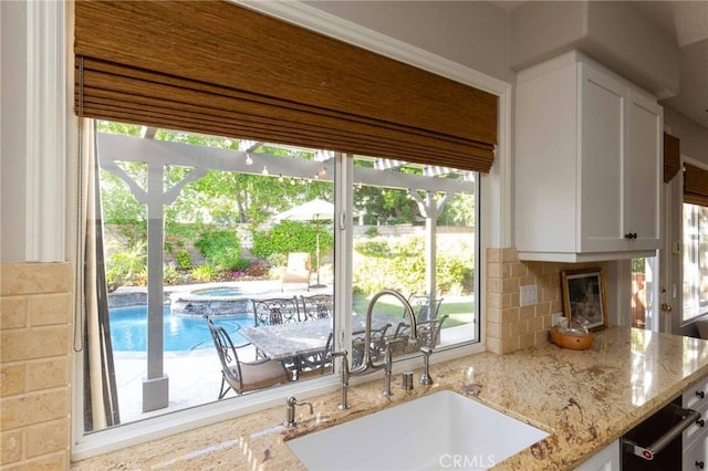 23317 Cuestport Dr, Valencia, CA 91354 - kitchen featuring a sink, white cabinets, tasteful backsplash, light stone counters, and a fireplace