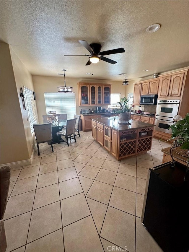 42500 20th St W, Lancaster, CA 93534 - kitchen with dark countertops, appliances with stainless steel finishes, a textured ceiling, glass insert cabinets, and light tile patterned flooring